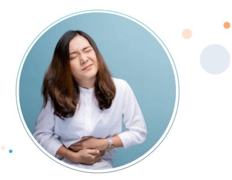 Mujer de mediana edad sentada en la cama con gesto de dolor abdominal